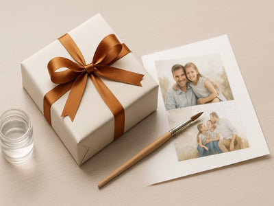 Gift box with brown ribbon, photo prints, and a pen on a beige surface