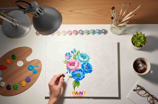 Top-down view of a paint by numbers floral artwork in progress, surrounded by paint pots, palette, brushes, and a cup of coffee.