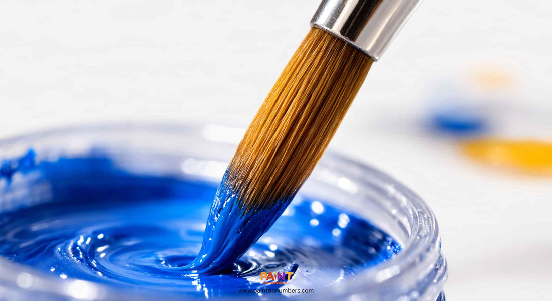 An extreme close-up showing a synthetic paint brush correctly loaded with blue acrylic paint only at the very tip, keeping the metal ferrule clean.