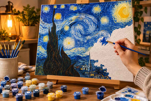 A hand holds a blue paintbrush while painting a canvas in the style of Van Gogh's Starry Night, set on a wooden easel with paint tubes and brushes around it in a cozy room.