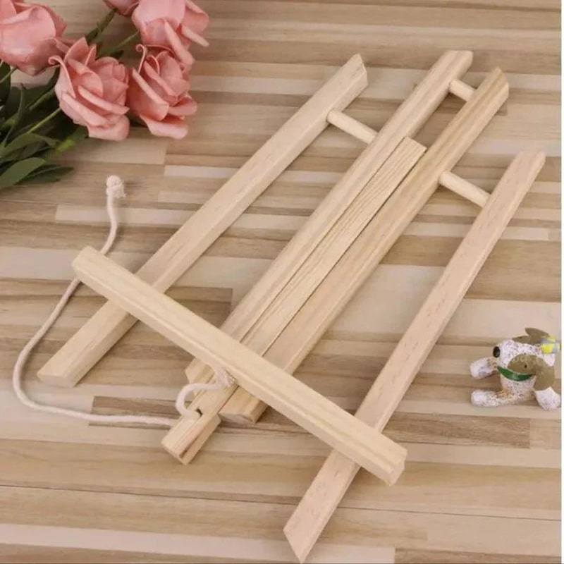 Wooden folding stand on a wooden surface with pink flowers and a small plant in the background.