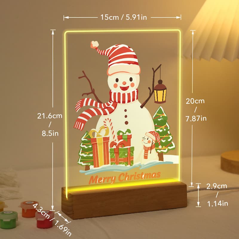 A glowing acrylic Christmas night light on a wooden base, showing a snowman with a red-and-white striped hat and scarf, gifts, trees, and the words 'Merry Christmas.' White dimension lines and text overlay the product, showing measurements in centimeters and inches.