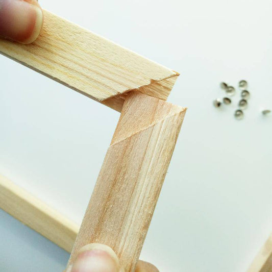 Wooden frame held by a hand with small screws on a light background