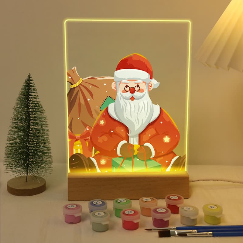 Decorative lamp with Santa Claus design on a table with paint cans and a brush.