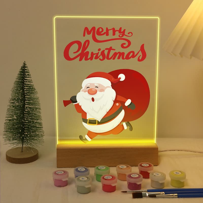 Decorative light box with Santa Claus illustration and 'Merry Christmas' text, surrounded by paint containers and a brush.